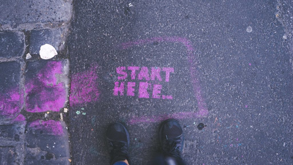 Shoes on blacktop with chalk that says "start here"