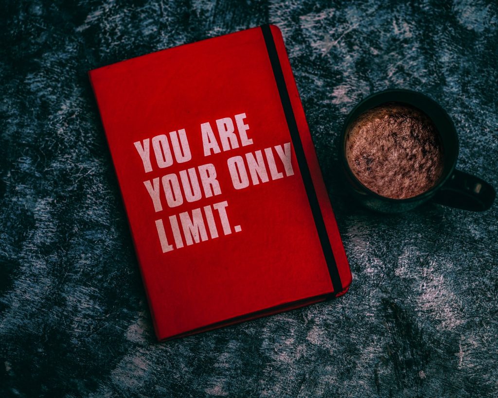 Red journal with the words, "you are your only limit" next to a cup of coffee